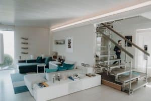 Ein moderner offener Wohnraum mit bodentfiefen Fenstern und einer Stahltreppe mit Glasgeländer im Musterhauspark.