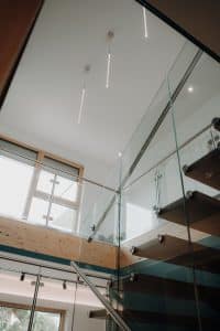 Treppenaufgang mit Glasgeländer, Galerie und drei minimalistischen Leuchtelementen im Musterhauspark.