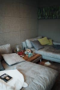 Ein Fernsehzimmer mit zwei Chaiselongues in hellgrauem Lederbezug, einem dazupassenden großen Couchtisch und deckenhohen, stoffbezogenen Akkustikpaneelen im Musterhauspark.