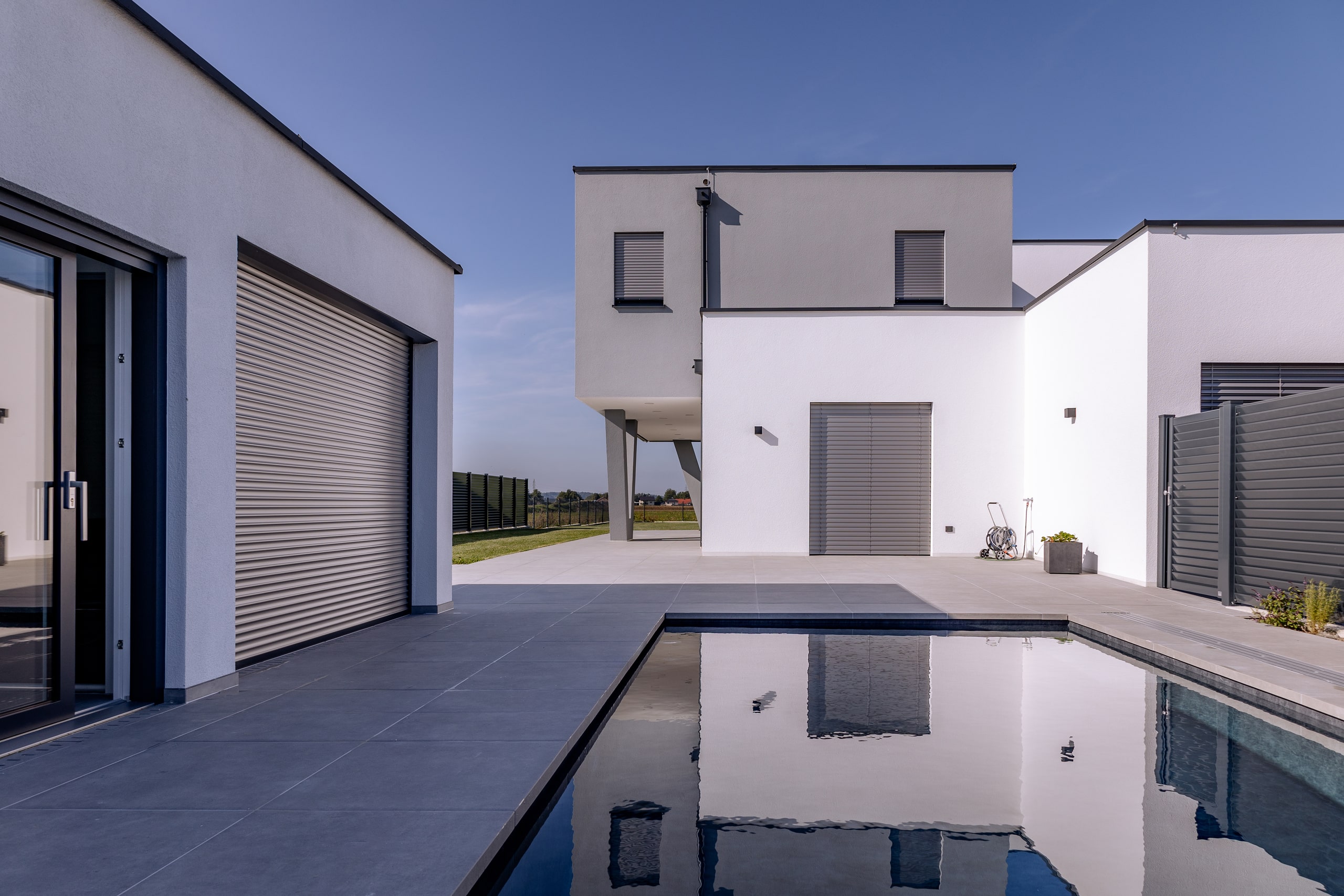 Modernes Flachdach-Wohnhaus mit Terrasse und Pool und zur Gänze geschlossenen silber Jalousien von Newo.