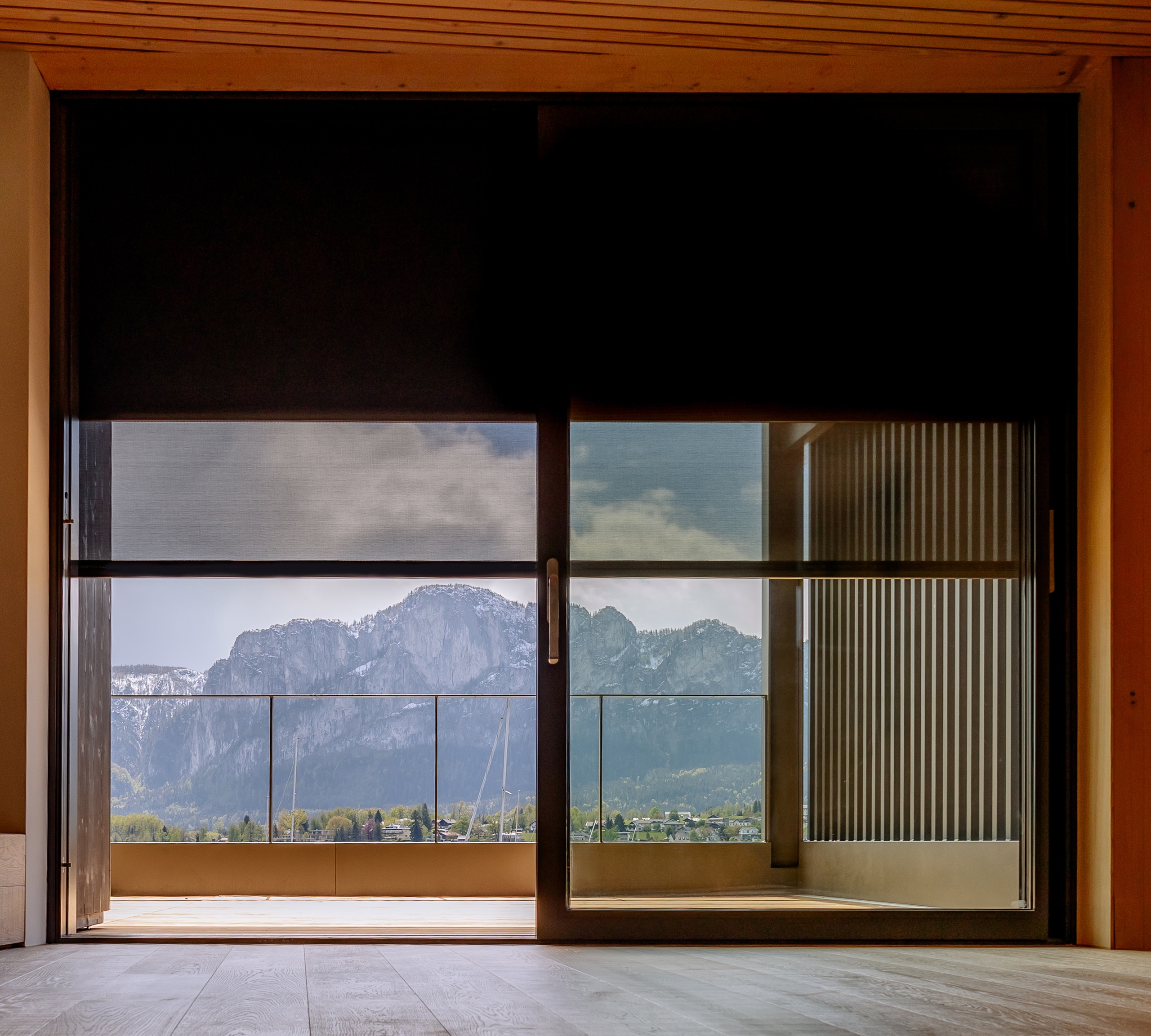 Große Glasfront mit Glasschiebetüre und textiler ZipTex Beschattung von Newo mit Blick auf Terrasse und Berge.