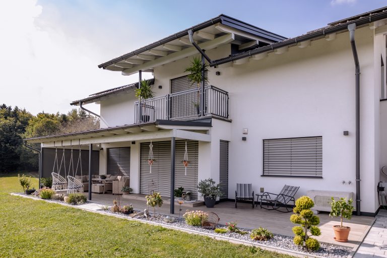 Newo Sonnen- und Insektenschutz zeigt ein Einfamilienhaus dessen Fenster und Terrassentüren mit Raffstore und Textilscreen beschattet werden.