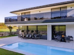 Modernes Einfamilienhaus mit Balkon und Glasgeländer, Pool, Terrasse und halb geöffneter Jalousie von Newo.