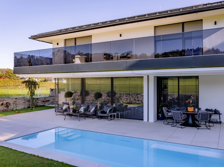 Modernes Einfamilienhaus mit Balkon und Glasgeländer, Pool, Terrasse und halb geöffneter Jalousie von Newo.