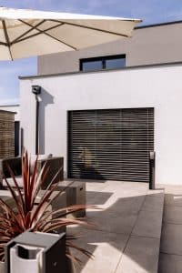 Newo Sonnen- und Insektenschutz zeigt eine Terrasse modernes Haus, dessen Terrassentür mit Raffstore beschattet wird.