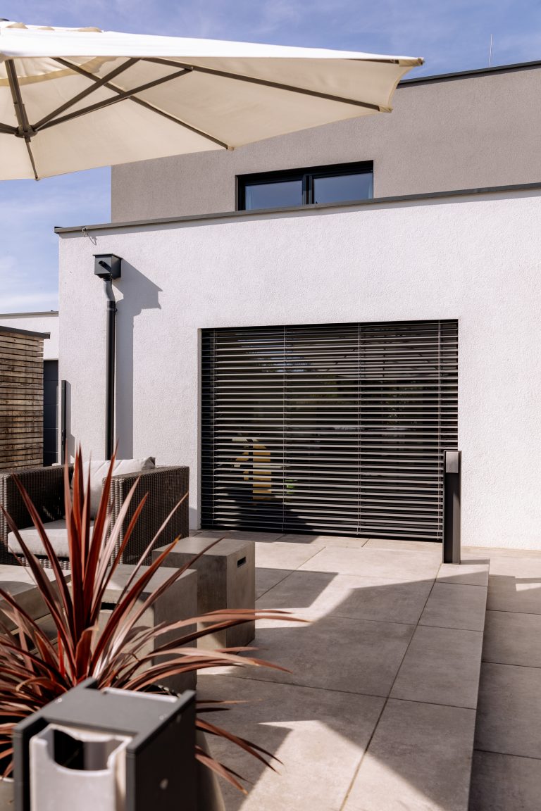 Newo Sonnen- und Insektenschutz zeigt eine Terrasse modernes Haus, dessen Terrassentür mit Raffstore beschattet wird.
