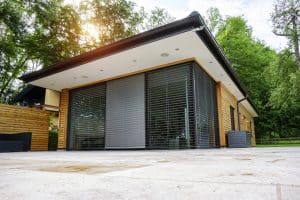 Newo Sonnen- und Insektenschutz zeigt ein Einfamilienhaus mit Terrasse und bodentiefen Fensterfronten, die mit Raffstores beschattet werden.