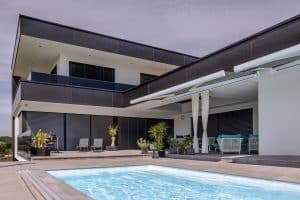 Newo Sonnen- und Insektenschutz zeigt ein Einfamilienhaus mit Terrasse und Pool und bodentiefe Fensterfronten, die mit Raffstores beschattet wird und zwei Markiesen.