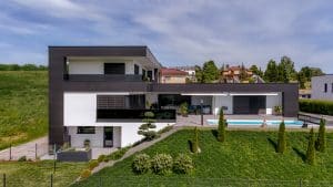 Newo Sonnen- und Insektenschutz zeigt ein Einfamilienhaus mit Flachdach, Terrasse mit Pool und bodentiefe Fensterfronten, die mit Raffstores beschattet werden.