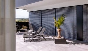 Newo Sonnen- und Insektenschutz zeigt eine Terrasse mit bodentiefer Fensterfront, die mit Raffstores beschattet werden.