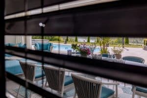 Newo Sonnen- und Insektenschutz zeigt eine Terrasse mit Pool durch ein Fenster, das mit Raffstores beschattet wird.