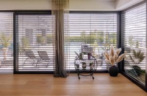 Newo Sonnen- und Insektenschutz zeigt einen Wohnraum, mit Blick auf die Terrasse durch eine Fensterfront mit Raffstores.