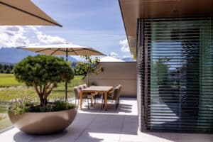 Großzügiger Balkonbereich einer Wohnung mit moderner Eckverglasung mit schwarzem Alu-Rahmen, halboffenen Raffstores von Newo.