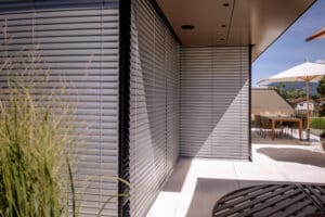 Großzügiger Balkonbereich einer Wohnung mit moderner Eckverglasung mit schwarzem Alu-Rahmen, geschlossenen silbernen Raffstores von Newo.