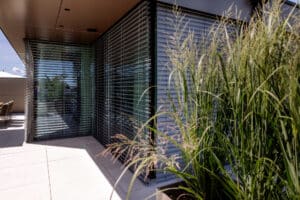 Wohnung mit moderner Eckverglasung mit schwarzem Alu-Rahmen und teils geschlossenen, teils offenen silbernen Raffstores von Newo.