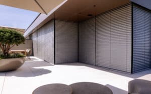 Eine Eckverglasung mit schwarzem Alu-Rahmen und außenliegenden, silbernen, geschlossenen Raffstores von Newo.