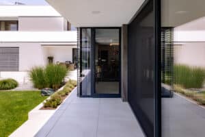 Terrassenbereich mit Verglasung und Terrassentüren mit schwarzem Alu-Rahmen, halbgeschlossenen Raffstores und und einer vorgeschobenen langen Insektenschutztüre von Newo.