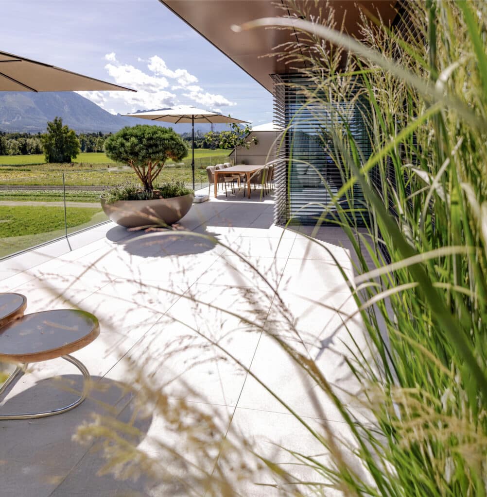 Großzügiger Terrassenbereich mit moderner Eckverglasung mit schwarzem Alu-Rahmen und halboffenen Raffstores von Newo.