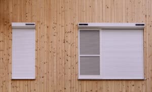 Ein Haus mit Holzfassadenverkleidung und Fenstern mit Vorbaurollladen in Weiss mit Solarmotor in Nahaufnahme von NEWO.