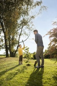 Vater und Kind beim Pflanzen eines Baumes in der Natur, gezeigt von ÖkoFEN.