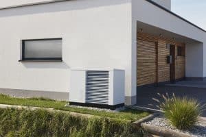 Einfamilienbungalow mit weissem Fassadenputz, einem überdachtem holzvertäfeltem Eingangsbereich mit passendem Garagentor und einer hellgrauen Wärmepumpe von ÖkoFEN.