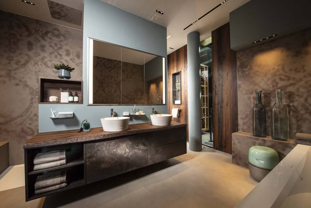 Modernes Badezimmer mit rustikalen Altholz-Elementen, Steinoptikfronten, dunklen schemenhaften Ornamentfliesen und türkisfarbenen Wandakzenten wirkt von HOLTER gezeigt von Limbach.