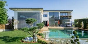 Villa mit Flachdach, privatem Hallenbad, einem großzügigem Garten, Terrasse mit Fliesen in Holzoptik und Naturpool mit Holzteg von Planungsbüro Schaufler.