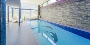 Private Schwimmhalle mit Indoorpool und Relaxliegen, Säulen mit blauen Mosaikfliesen und Wandfliesen in Steinoptik von Planungsbüro Schaufler.