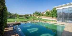 Garten und Terrasse einer Villa mit Naturpool und einer Poolumrandung und Aussenfliesen in Holzoptik mit Bodenspots einem Gartenbonsai, einem Hügel und einem Kiesweg von Planungsbüro Schaufler.