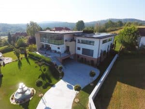 Villa mit Flachdach, dachmontierten Solarpaneelen, Garage, überdachter Terrasse und einer großzügigen Auffahrt und Vorgarten mit Brunnen aus der Vogelperspektive von Planungsbüro Schaufler.