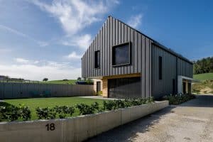 Modernes Einfamilienhaus mit Satteldach, Gartenfläche, überdachter Terrasse, bodentiefen Fenstern, Terrassentüren, Jalousien und Fassaden- und Bauelementen aus Holz und Beton von Planungsbüro Schaufler.