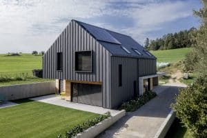 Einfamilienhaus mit Satteldach, dachmontierter Solaranlage, Blechverkleidung, Bau- und Fassadenelementen aus Beton und Holz und einem großen Garten von Planungsbüro Schaufler.