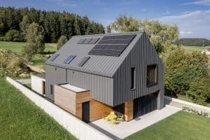 Einfamilienhaus mit Satteldach, dachmontierter Solaranlage, Dachfenstern, Terrasse mit integrierter Überdachung, Blechverkleidung, Bau- und Fassadenelementen aus Beton und Holz und einem großen Garten von Planungsbüro Schaufler.