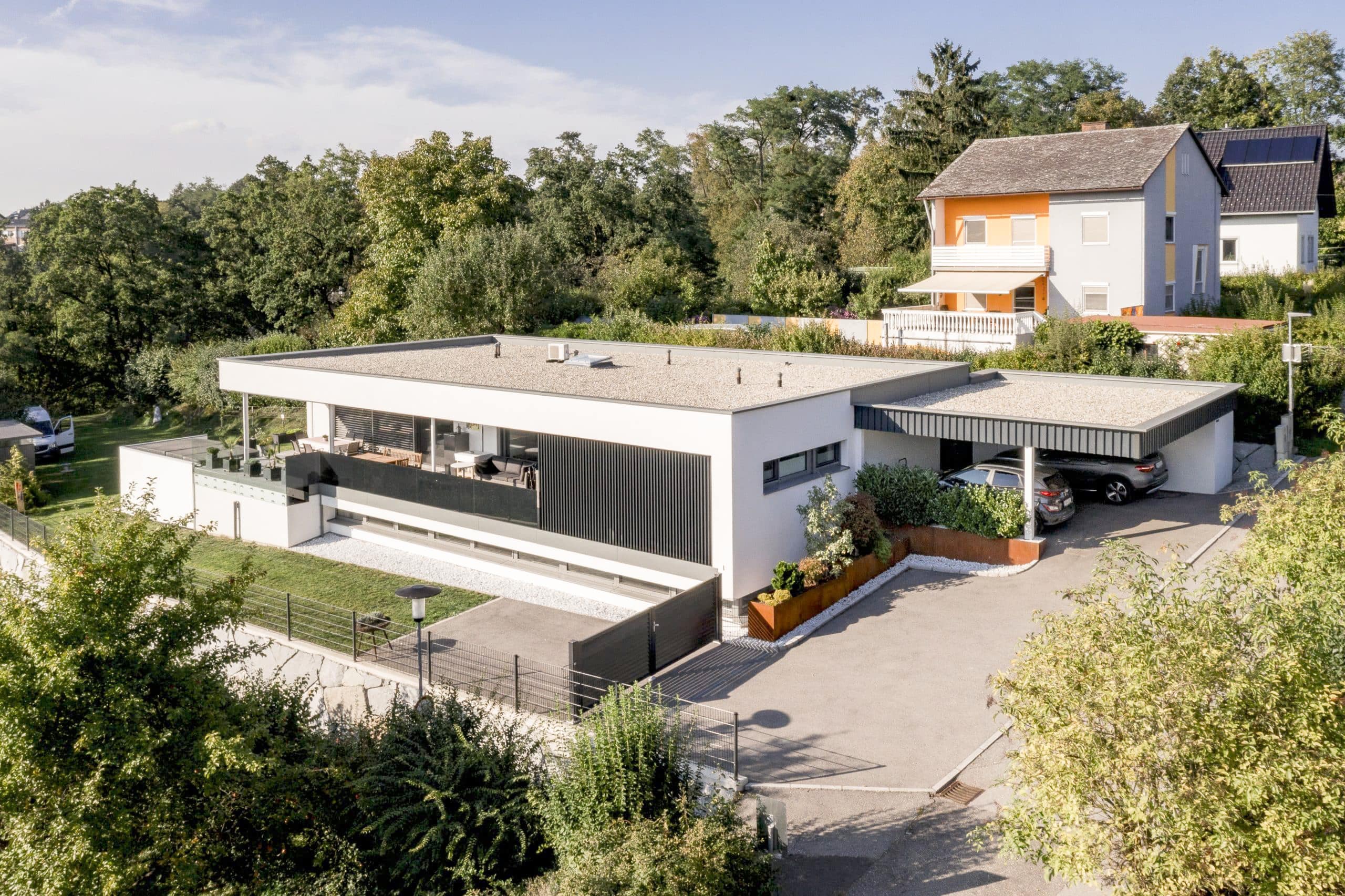 Flachdachbungalow aus der Vogelperspektive mit überdachter Terrasse, schwarzem Glasgeländer und Carport von Planungsbüro Schaufler.