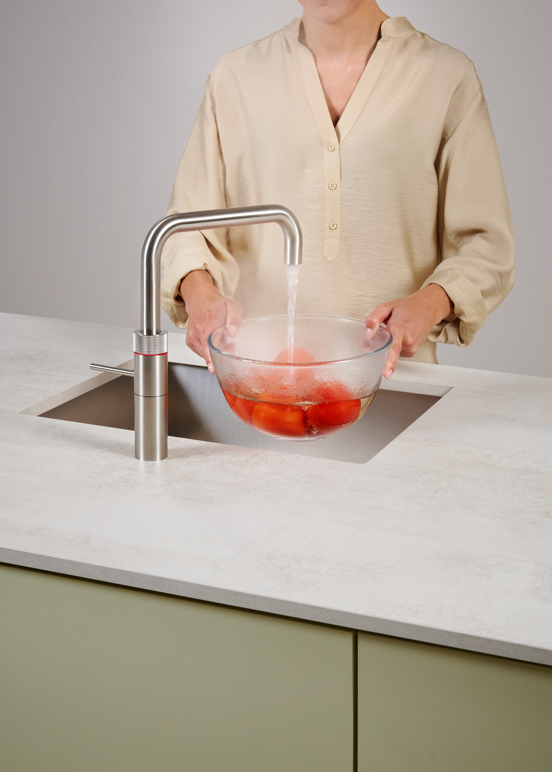 Eine Frau blanchiert Tomaten mit dem kochenden Wasser der Armatur Fusion Square aus rostfreiem Stahl von Quooker.