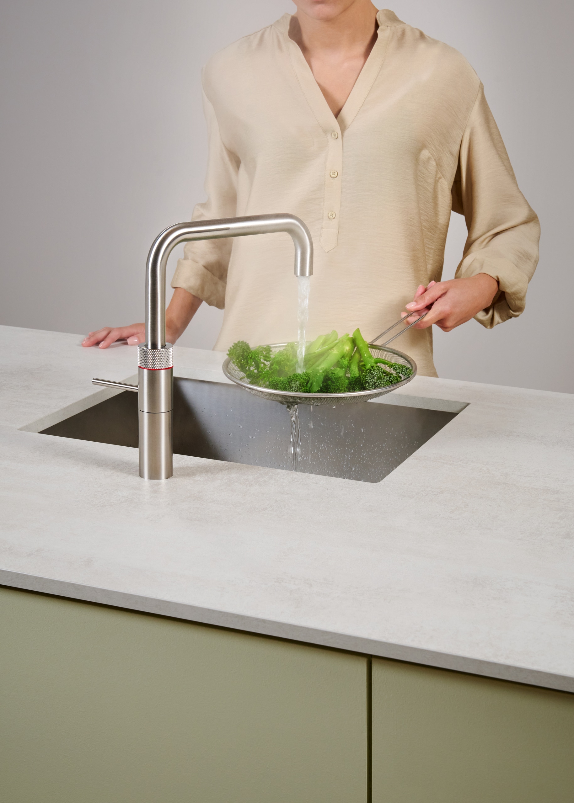 Eine Frau blanchiert Brokkoli mit dem kochenden Wasser der Armatur Fusion Square aus rostfreiem Stahl von Quooker.