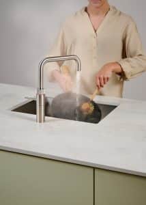 Eine Frau schrubbt eine Pfanne mit dem kochenden Wasser der Armatur Fusion Square aus rostfreiem Stahl von Quooker.
