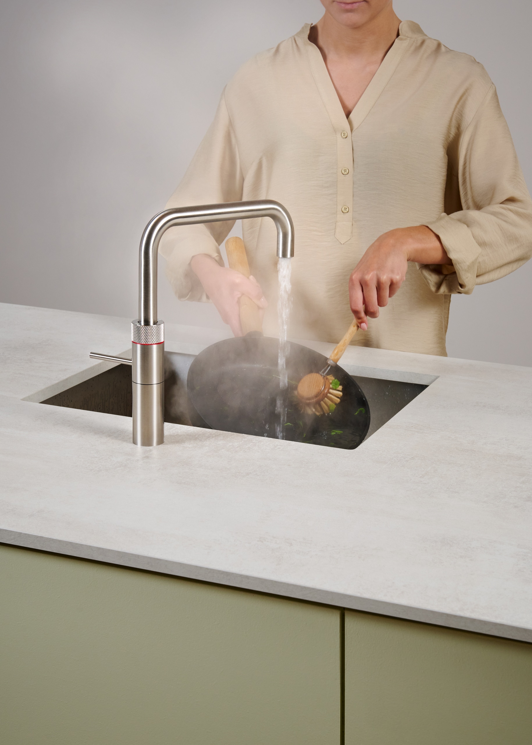 Eine Frau schrubbt eine Pfanne mit dem kochenden Wasser der Armatur Fusion Square aus rostfreiem Stahl von Quooker.