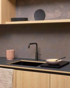 Eine moderne Küchenzeile mit Rückwand in Anthrazit, Küchenfronten in hellem Holz mit einem passenden, offenen Küchenoberregal, einer schwarzen Arbeitsfläche mit quadratischer Spüle und einer Quooker Fusion Square-Armatur in "Gunmetal".