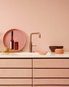 Eine moderne Küche komplett in Rosa mit passenden Küchenfronten, Rückwand, Accessoires einer weissen Arbeitsfläche mit gegossener Spüle und einer Quooker Fusion Square-Armatur in "Kupfer Rosé" mit passendem Einbau-Seifenspender.