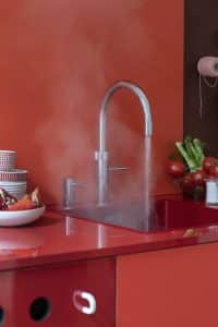 Eine leuchtend rote Küche in Lackoptik mit roter Rückwand und einer Quooker Fusion-Armatur in Chrom aus der kochendes Wasser strömt.