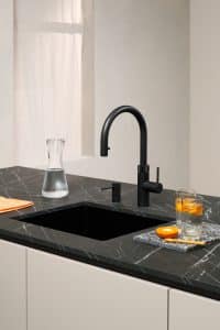 Küche im Schwarz-Weiss-Look mit einer Kücheninsel mit schwarzen Marmorarbeitsplatte, weissen Fronten und einer Armatur mit C-Auslauf und passendem Seifenspender in "black" von Quooker.