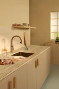 Ein “Quooker Flex Round”-Wasserhahn in Patina‑Messing in einer beigen Küche mit Holzakzenten und Steinarbeitsplatte von Quooker.