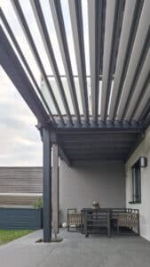 Eine anthrazitfarbene Pergola mit halbgeöffnetem Lamellendach auf einer graugefliesten Terrasse von Sonnenschutz Rachbauer.