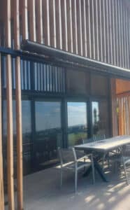 Ein Haus mit Holzfassade, gemauertem Terrassenpodest und einer im eingezogenen Zustand fast unsichtbaren Gelenkarmmarkise mit schwarzem Rahmen von Sonnenschutz Rachbauer.