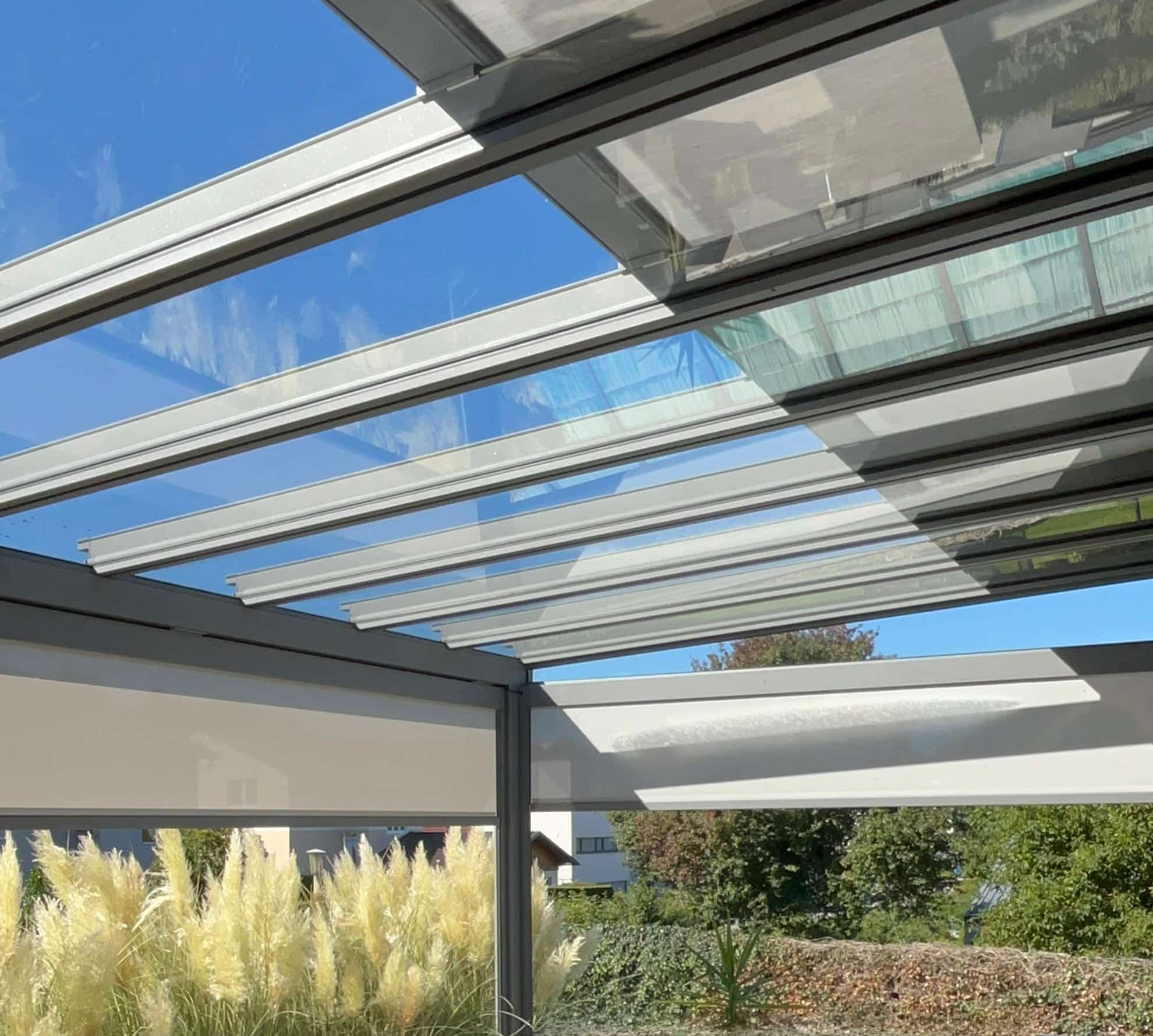 Ein Sommergarten bzw. Pergola mit Outdoorlounge, Glasdach und Senkrechtmarkisen umgeben von einem wilden, blühenden Garten von Sonnenschutz Rachbauer.