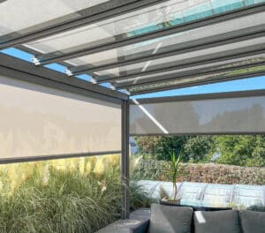 Ein Sommergarten bzw. Pergola mit Outdoorlounge, Glasdach und Senkrechtmarkisen umgeben von einem wilden, blühenden Garten von Sonnenschutz Rachbauer.