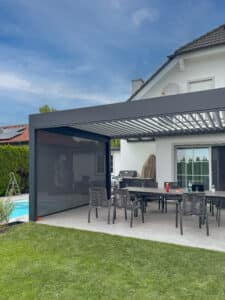 Anthrazitfarbene Lamellen-Pergola mit halboffenen Dachlamellen und seitlich integriertem Insektenschutz von Sonnenschutz Rachbauer.