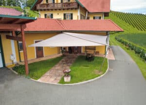 Beiges Sonnensegel gespannt an vier Seiten im Vorgarten eines alten Hofes von Sonnenschutz Rachbauer.