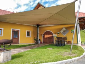 Beiges Sonnensegel gespannt an vier Seiten im Vorgarten eines alten Hofes von Sonnenschutz Rachbauer.